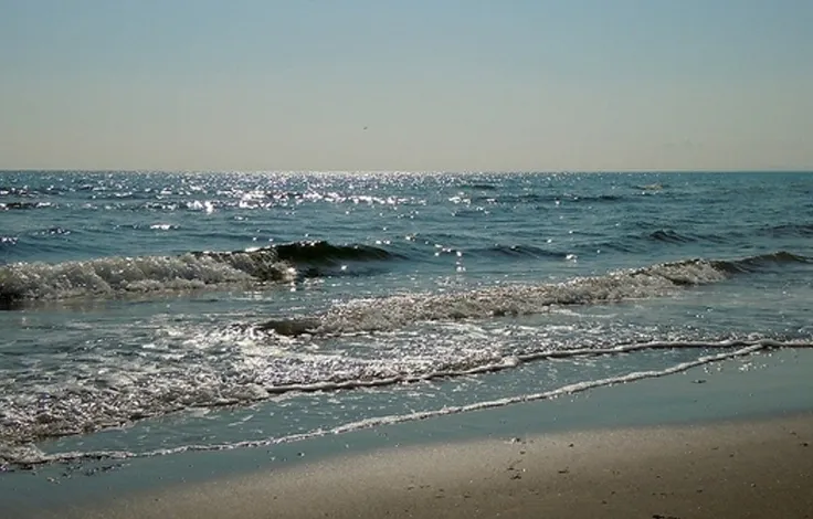 Wellen laufen an einem Strand aus, dahinter das offene Meer